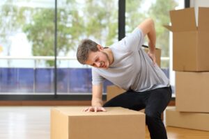 A man experiencing back pain as he moves boxes in his recently acquired home.