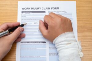 Completing a work injury claim form with a hand wrapped in a medical context, emphasizing insurance and workplace injury concepts.