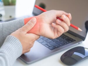 Close-up of a woman experiencing wrist pain due to prolonged computer usage, illustrating the concept of office syndrome.