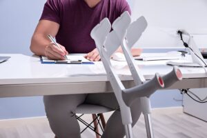 Close-up Of Crutches Leaning On Table In Front Of Handicapped Man Filling Form