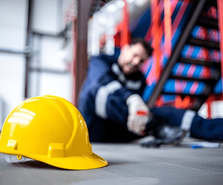 Safety at work. Close up view on hardhat and injured factory worker in background.